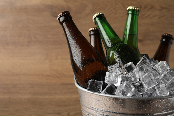 Metal bucket with beer and ice cubes on wooden background. Space for text - Foto, imagen