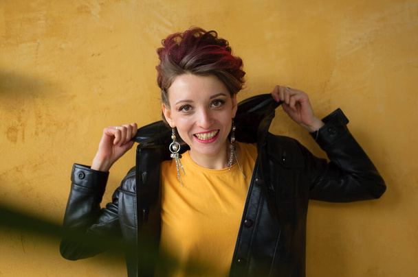 Lumoava nainen punk rock-tyyliin puolueen vaatteet tummanpunaiset hiukset rento mekko, musta nahkatakki, ja pitkät korvakorut keltaisella taustalla
 - Valokuva, kuva