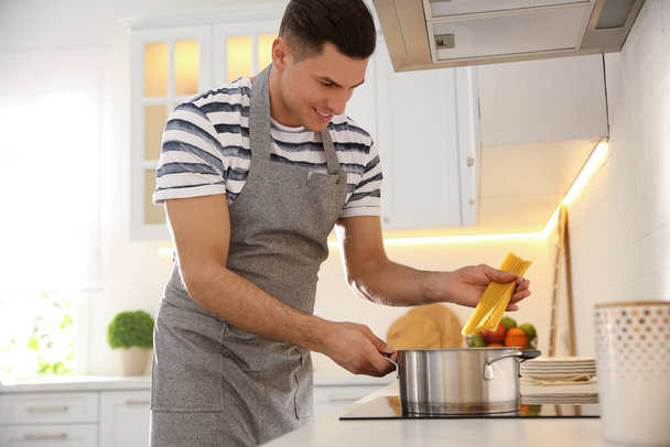 Handsome man cooking pasta on stove in kitchen - Foto, Imagem