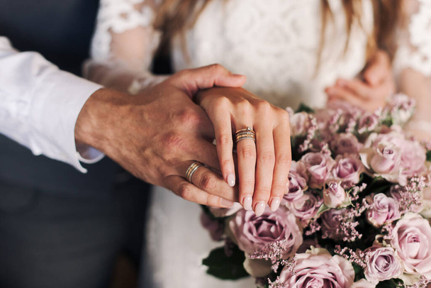 The hands of the newlyweds. The hands of the bride and groom against the background of a bouquet. Wedding rings in the hands.  - Zdjęcie, obraz