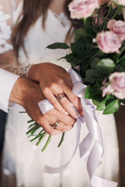 The hands of the newlyweds. The hands of the bride and groom against the background of a bouquet. Wedding rings in the hands.  - Photo, Image