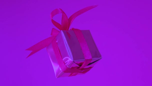 Ajándékdoboz piros szalaggal, neon lila háttérrel. 360 fokos elfordulás - Felvétel, videó