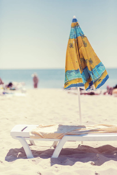 Summer vertical composition of a beach umbrella and deck chair with a carelessly thrown beach towel. Sun sand sea and beach - Photo, Image