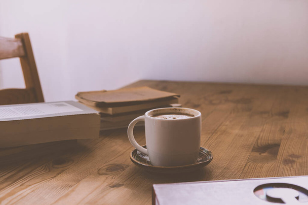 白いカップにカプチーノコーヒーと一連の本が添えられた素朴な木製のテーブル - 写真・画像