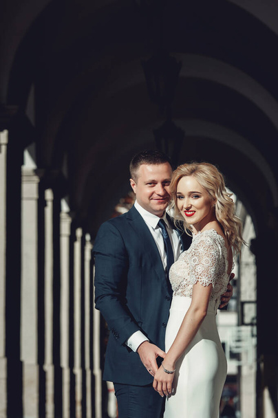 Cheerful wedding couple posing on a street of an old down. Portrait of Beautiful Happy Curly Blond Hair Bride - Фото, изображение