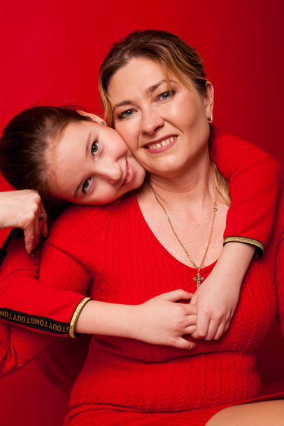 portret van mooie moeder met dochter op een rode achtergrond - Foto, afbeelding