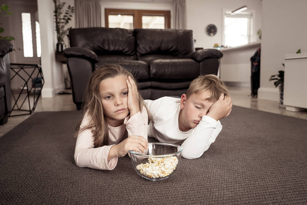 Coronavirus lockdow. Bored little girl and sad boy watching tv in isolation at home during quarantine COVID 19 Outbreak. Mandatory lockdowns and school closures impact on children mental health. - Photo, Image