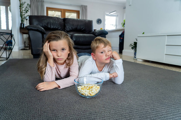 Coronavirus lockdow. Bored little girl and sad boy watching tv in isolation at home during quarantine COVID 19 Outbreak. Mandatory lockdowns and school closures impact on children mental health. - 写真・画像