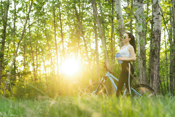 Jeune femme agréable a une balade à vélo dans un parc au coucher du soleil. espace de copie
 - Photo, image