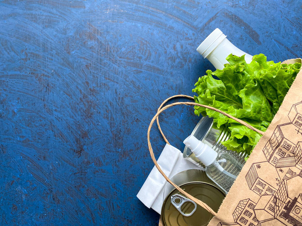 Papieren zak met voedsel, antiseptisch en medisch masker op een blauwe achtergrond. Voedsellevering, donatie. Vrije ruimte. - Foto, afbeelding