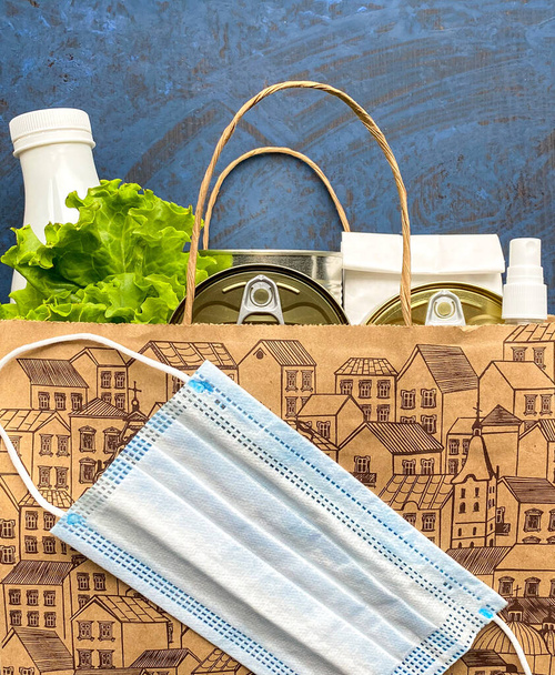 Papírový sáček s jídlem, antiseptickou a lékařskou maskou na modrém pozadí. Dodávka jídla, darování. Volné místo. - Fotografie, Obrázek