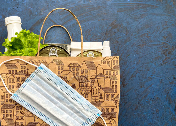 Papieren zak met voedsel, antiseptisch en medisch masker op een blauwe achtergrond. Voedsellevering, donatie. Vrije ruimte. - Foto, afbeelding