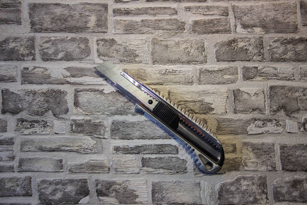 Kancelářský nůž na cihlovém pozadí. Pozadí jako textura - Fotografie, Obrázek
