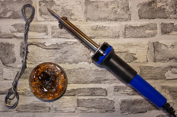 Soldering iron with a blue handle, rosin and soldering tin on a brick wall backgroun - Photo, Image