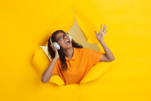 Cheerful young woman poses in torn yellow paper hole background, emotional and expressive - Foto, Imagem