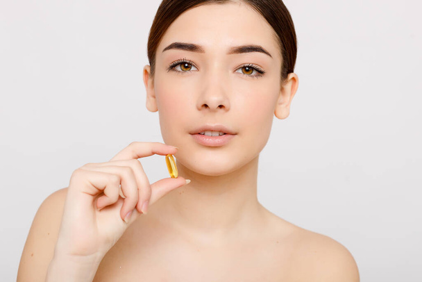 Healthy diet food. Beautiful smiling young woman holding a fish oil pill in her hand. Closeup. taking capsule. Vitamin and dietary supplements - Fotografie, Obrázek