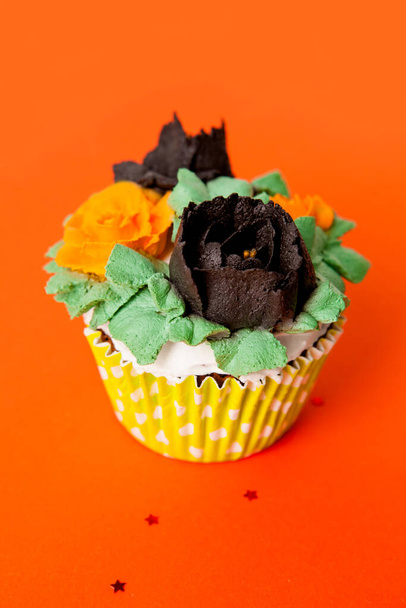 cupcake halloween decorado com rosas creme de laranja e preto em um fundo laranja
 - Foto, Imagem