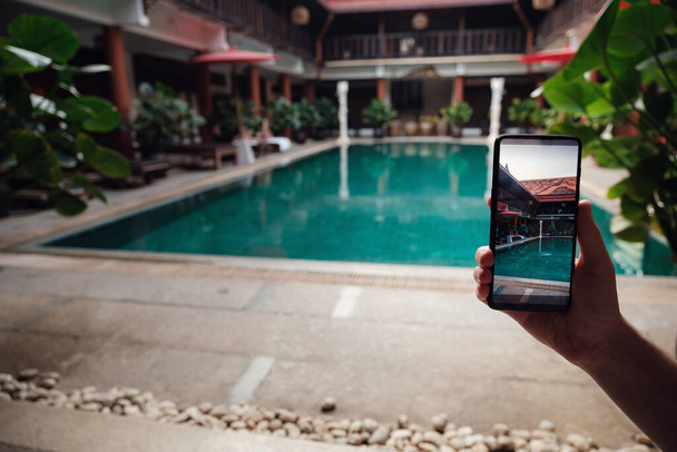 main tenant le téléphone sur le fond de la piscine à l'hôtel. appareil photo à l'écran. fermer main tenir smartphone prendre une photo des vacances d'été
. - Photo, image