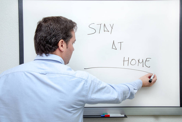 Volwassen man in blauw shirt schrijft op whiteboard Blijf thuis - Foto, afbeelding