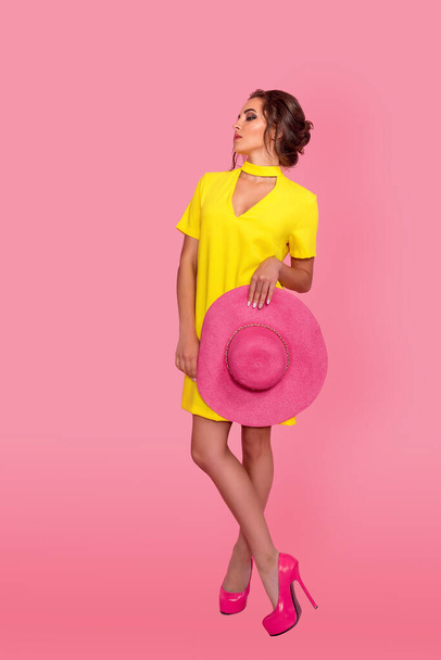 Молодая улыбающаяся женщина в жёлтом платье смотрит на камеру в розовом пространстве. Полнометражный снимок. Полный портрет красивой улыбающейся женщины в платье. изолированные
 - Фото, изображение