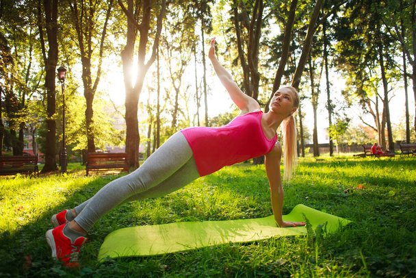 Young athletic girl doing fitness exercises in a summer green park, training day for taking care of health in nature - Zdjęcie, obraz