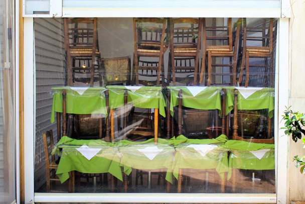 Athen, Griechenland, 6. Mai 2020 - Tische und Stühle stapeln sich während der Sperrung des Coronavirus vor einem geschlossenen Café-Restaurant. - Foto, Bild