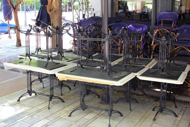 Athens, Greece, May 6 2020 - Tables and chairs stacked outside closed cafe-restaurant during the Coronavirus lockdown. - Photo, Image
