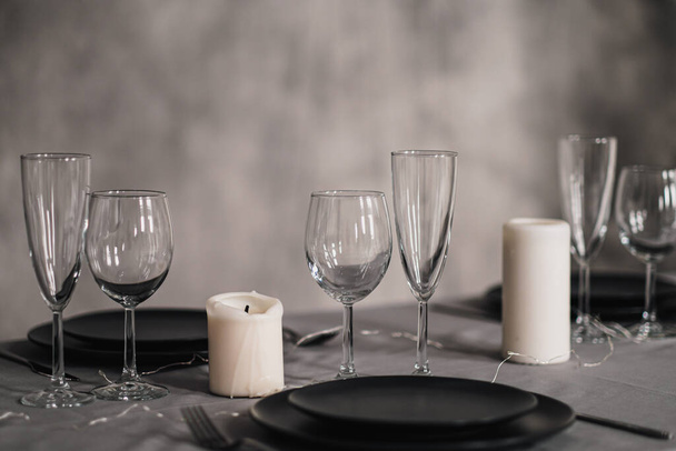 A table set in the restaurant. Serving a table. Grey artistic background. Black matte utensils, glass glasses. White candles and decor. - Photo, image