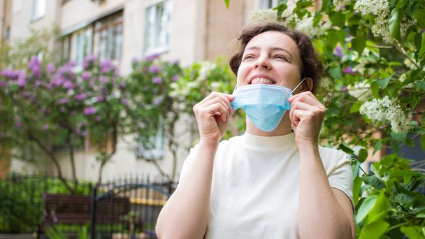 Quarantine is over concept. Smiling happy woman taking off medical protective mask outdoor. Freedom. Breathe deep. We are safe. We won. End of quarantine, isolation.  - Photo, Image