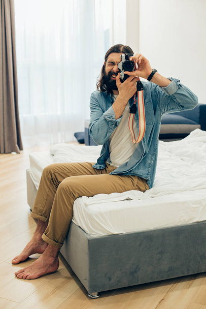Gladsome man looking happy while sitting at home and taking photos on his favorite camera - Photo, Image