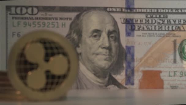 Gold coin of the future Ripple XRP on the foreground and bill of 100 american dollar on the background. Focus swich from cryptocoin to USD. Macro close-up shot. 4K video - Materiał filmowy, wideo