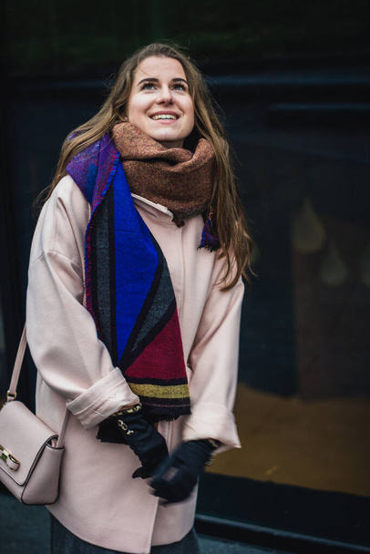 Schöne stylische junge Frau in einem warmen Schal Blue Jeans trendigen gemütlichen Mantel posiert allein vor verlassenen Hof in Herbst Stadt Outfit. Berührt ihre Haare. Retro-Filter bearbeiten. - Foto, Bild