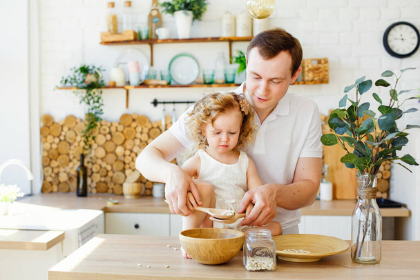 Masadaki parlak İskandinav tarzı mutfakta küçük bir kız çocuğu oynuyor. Baba ve kızı mısır ezmesiyle oynuyorlar. Montessori eğitimi kavramı. Eko mutfak. - Fotoğraf, Görsel