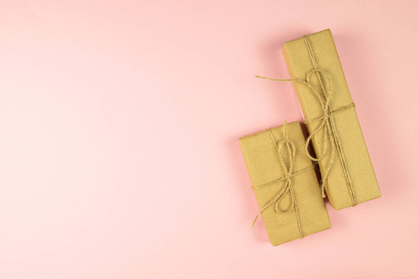 Two gift boxes wrapped of craft paper and burlap ribbon on the pink background, top view with clear space. - Фото, зображення