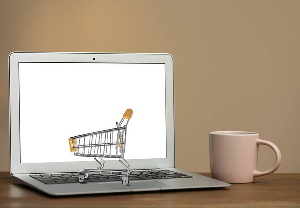Online shopping. Laptop with small cart and cup on table - Photo, Image
