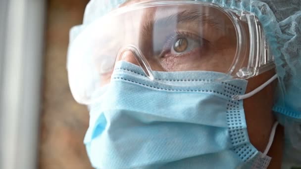 A woman in a medical mask, glasses and a cap looks into the distance - Video