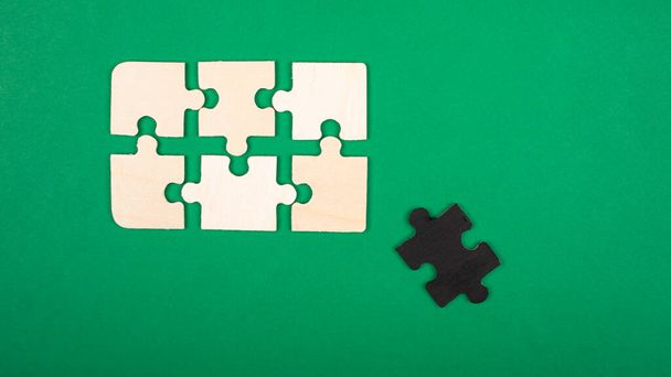 Teile der Puzzlefarben Weiß und Schwarz liegen auf grünem Hintergrund. Ausgestoßene asoziale weiße Krähe Nahaufnahme von oben - Foto, Bild
