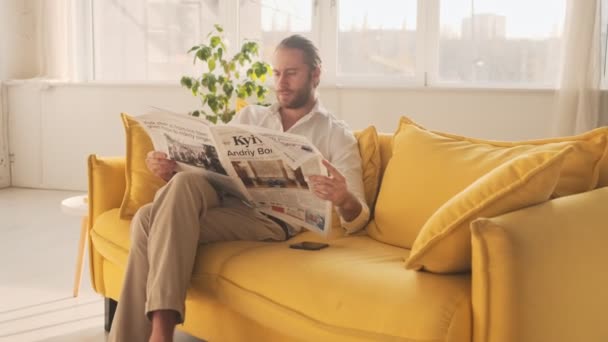A stylish handsome young man is reading a newspaper in the living room at home - Video