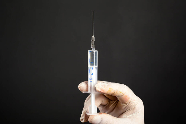 entregar uma luva branca estéril descartável segurando uma seringa médica 5 ml em um fundo escuro close-up. tiro um tratamento por injeção
 - Foto, Imagem