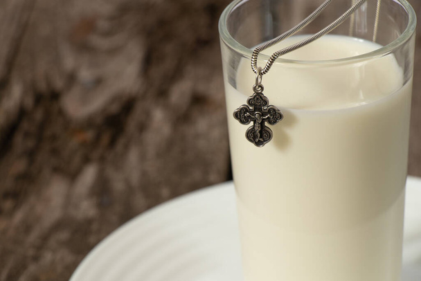 srebrny krzyż i szklanka mleka na drewnianym stole - Zdjęcie, obraz