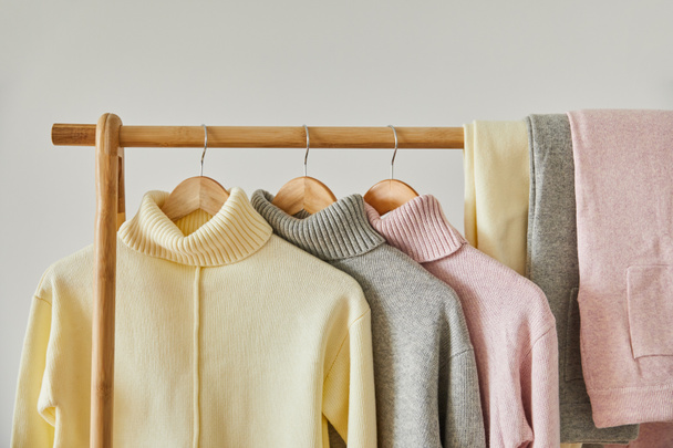 close up view of pink, beige and grey knitted soft sweaters and pants hanging on wooden rack isolated on white - Photo, Image