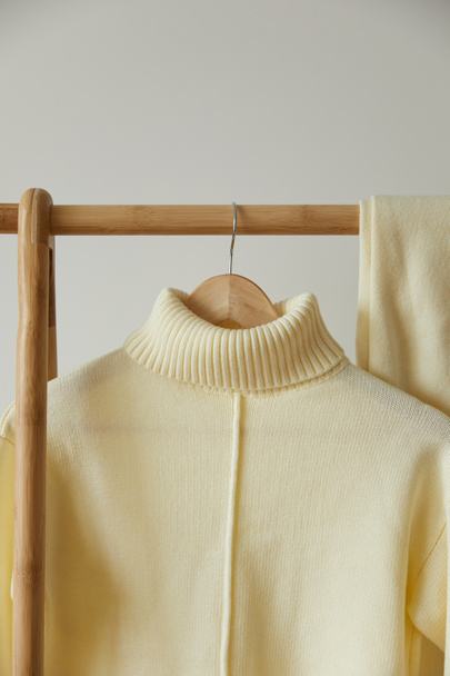 vista de cerca de jersey suave de punto beige y pantalones colgando en percha de madera aislado en blanco
 - Foto, Imagen