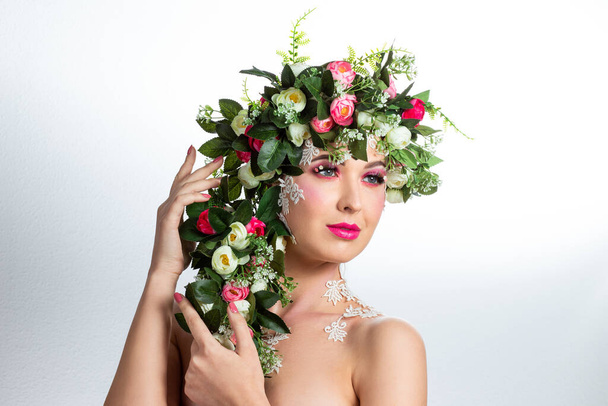 Portrait of a beautiful brunette with huge erect eyelashes in the image of spring with a wreath of roses on his head on a white background. - Fotografie, Obrázek