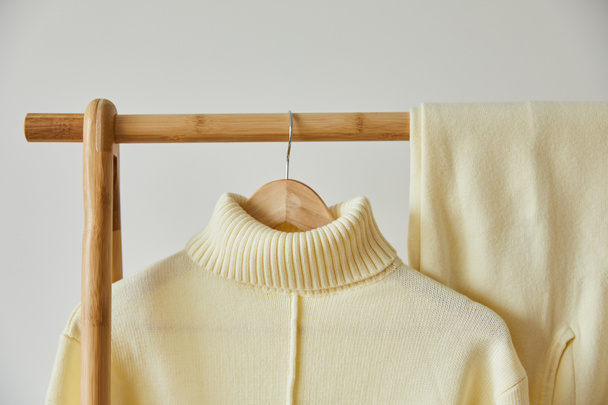close up view of beige knitted soft sweater and pants hanging on wooden hanger isolated on white - Foto, afbeelding