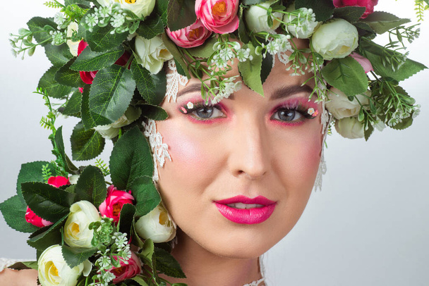 Portrait of a beautiful brunette with huge erect eyelashes in the image of spring with a wreath of roses on his head on a white background. - Foto, afbeelding