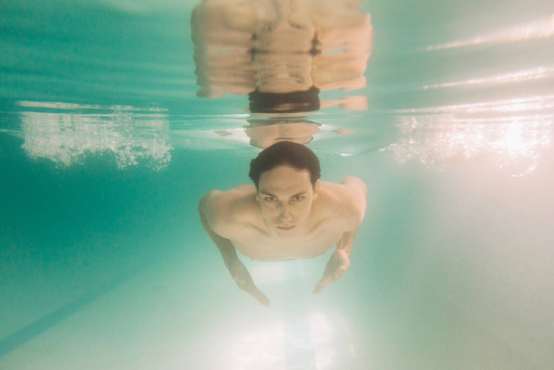 Fekete fürdőruhás férfi oktató úszik a víz alatt. - Fotó, kép
