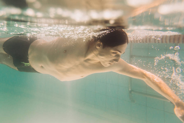man instructeur in zwart zwembroek is zwemmen onder water - Foto, afbeelding