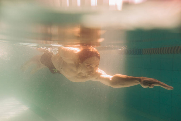 Мужчина-инструктор в черных плавках плавает под водой
 - Фото, изображение