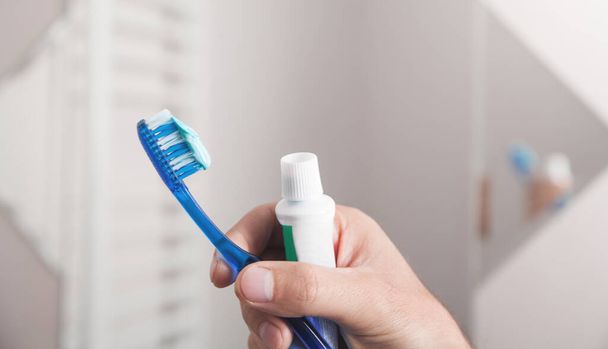 Mannelijke hand houden tandenborstel en tandpasta in de badkamer. - Foto, afbeelding