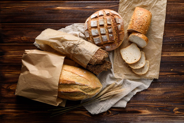 Horní pohled na různé druhy chutného čerstvě upečeného chleba v papírových sáčcích na dřevěném rustikálním stole. - Fotografie, Obrázek